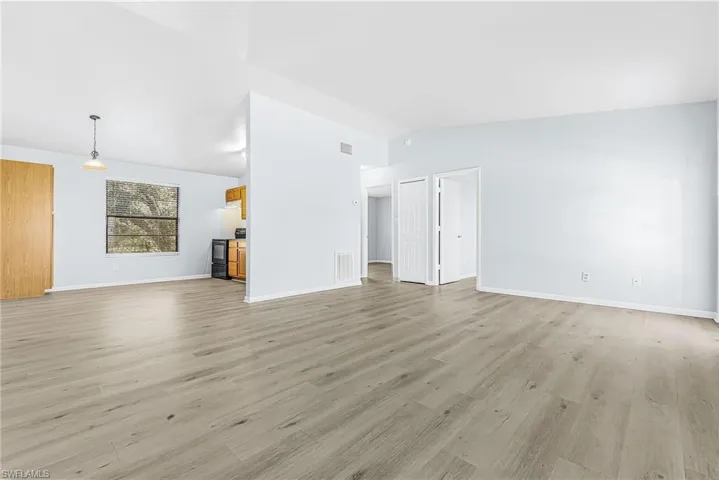 Expansive open-concept living area featuring wood-finish flooring, vaulted ceilings, and light-toned wall paint