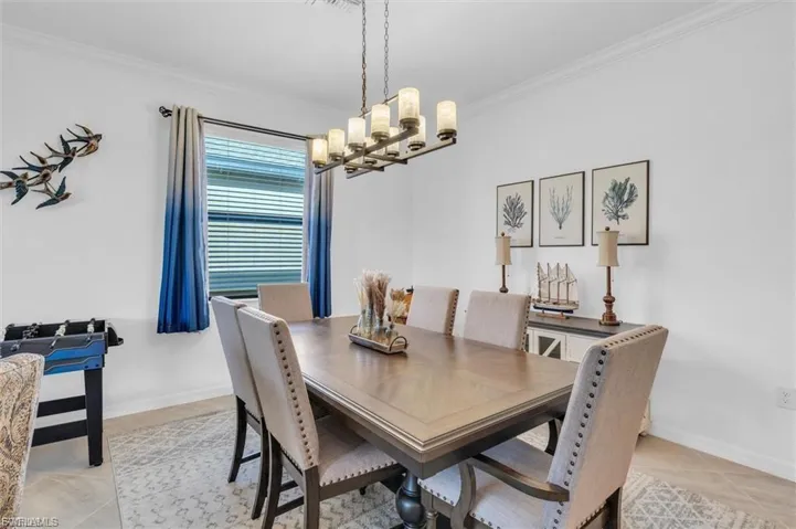 Dining area featuring crown molding, neutral wall finishes, and a linear chandelier with twelve glass-shaded lights