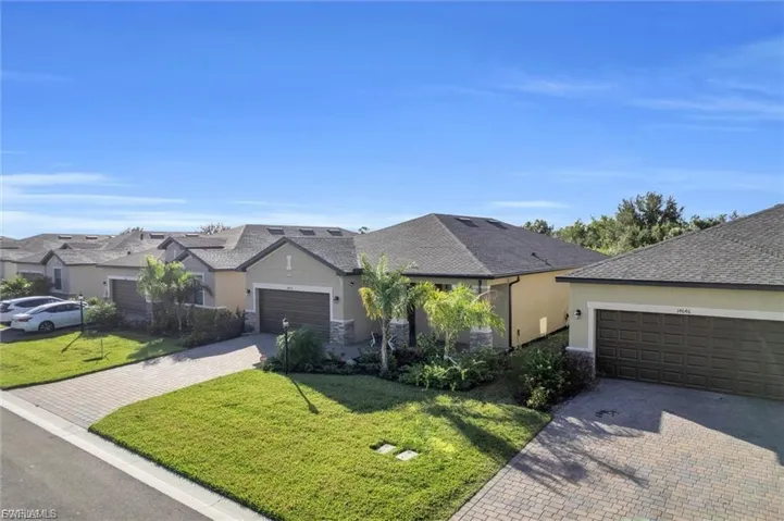 Stucco exterior with stone veneer accents, multi-gabled roofline, paver driveway, attached multi-car garages, and professional landscaping