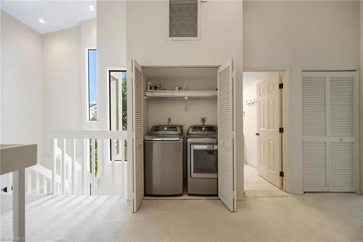 Laundry room with light colored carpet, electric dryer hookup, and a towering ceiling