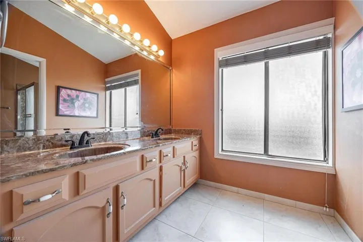 Bathroom featuring double sink vanity, vaulted ceiling, and tile patterned flooring