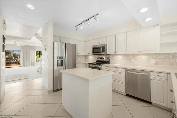 Kitchen featuring light tile patterned flooring, white cabinetry, backsplash, a kitchen island, and appliances with stainless steel finishes