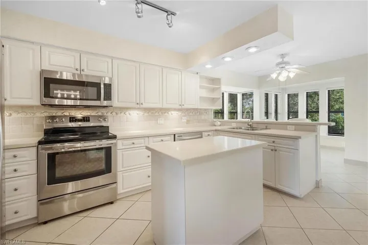 Kitchen featuring white cabinetry, ceiling fan, stainless steel appliances, a center island, and track lighting