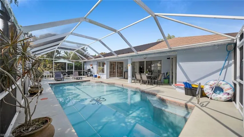 Screened swimming pool enclosure featuring a rectangular pool with patterned tile work, concrete decking, and direct access to the interior via sliding glass doors