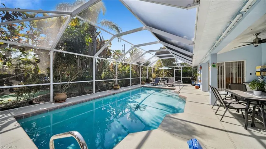 Screened pool enclosure with a geometric-shaped pool, concrete decking, and tropical landscaping
