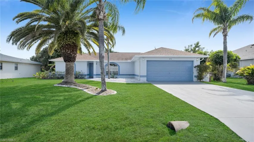 Single-story residence featuring a two-car garage, concrete driveway, lush green lawn, mature palm trees, and a tiled roof