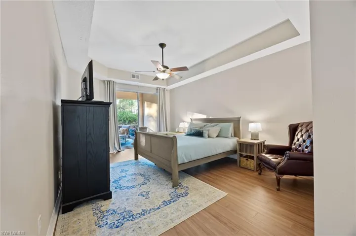 Bedroom with a raised ceiling, access to outside, light wood finished floors, and a ceiling fan
