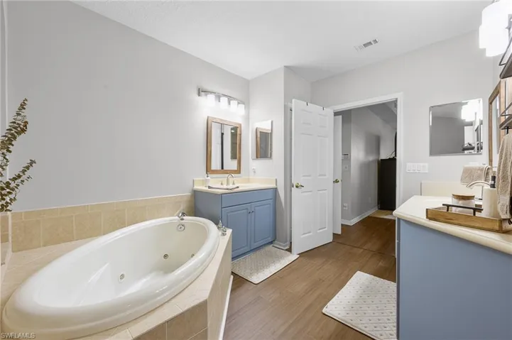 Bathroom with two vanities, a tub with jets, and light wood-style flooring