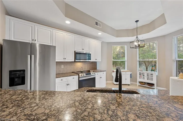 Kitchen with dark stone countertops, stainless steel appliances, white cabinets, a raised ceiling, and recessed lighting