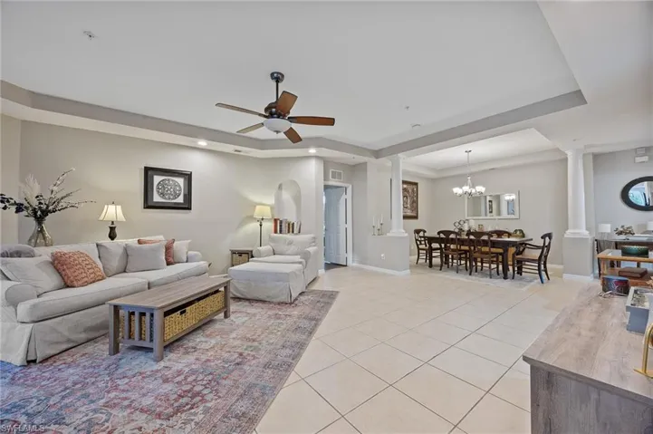 Living room featuring a tray ceiling, a chandelier, light tile patterned floors, recessed lighting, and a ceiling fan