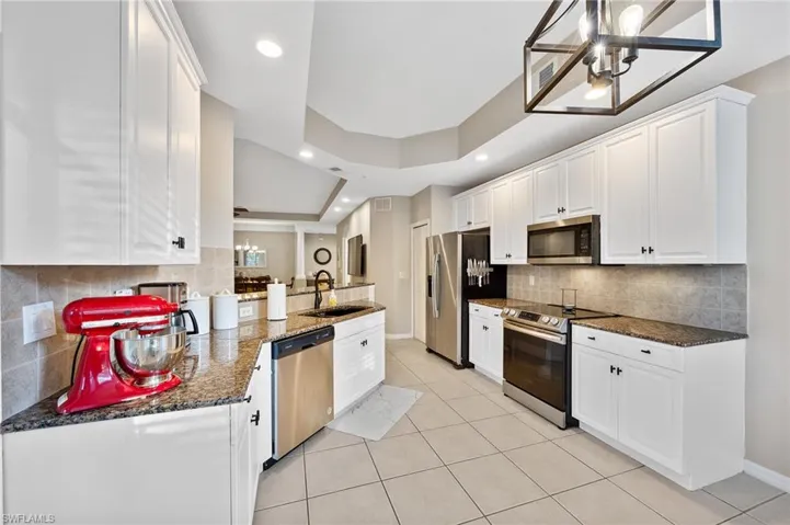 Kitchen with stainless steel appliances, dark stone counters, white cabinetry, light tile patterned flooring, and backsplash