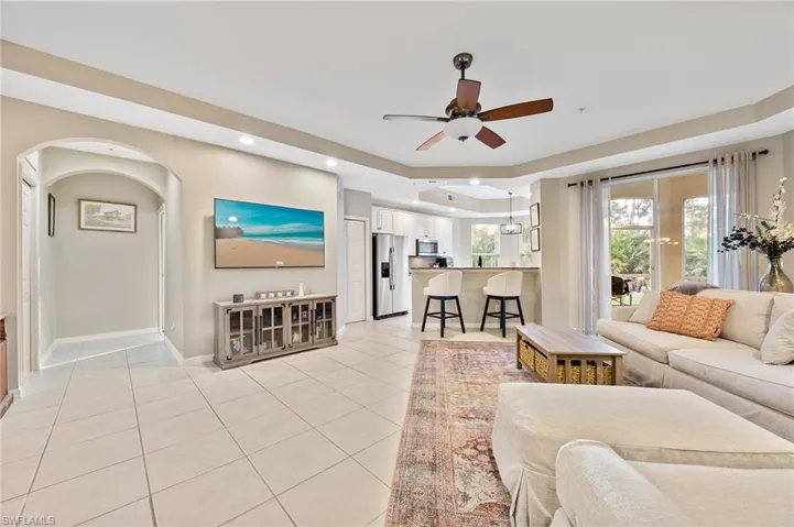 Living area with ceiling fan, light tile patterned floors, recessed lighting, arched walkways, and a tray ceiling