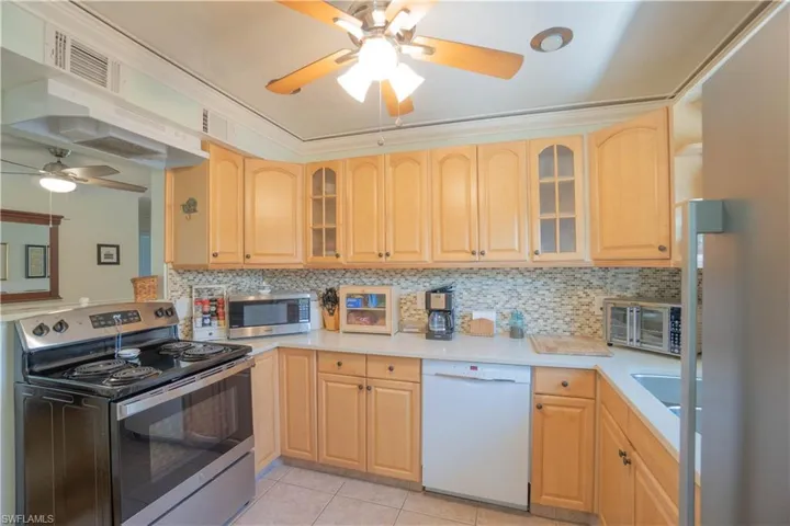 Kitchen featuring appliances with stainless steel finishes, glass insert cabinets, under cabinet range hood, and ceiling fan