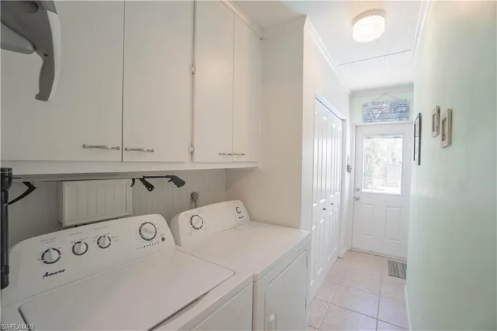 Laundry room featuring ornamental molding, light tile patterned floors, washing machine and clothes dryer, and cabinet space