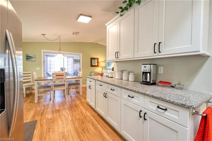 Kitchen with stainless steel fridge, light wood-type flooring, vaulted ceiling, pendant lighting, and white cabinets