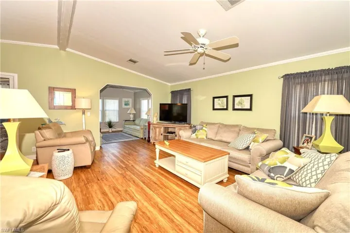 Living room with crown molding, ceiling fan, hardwood / wood-style floors, and lofted ceiling with beams