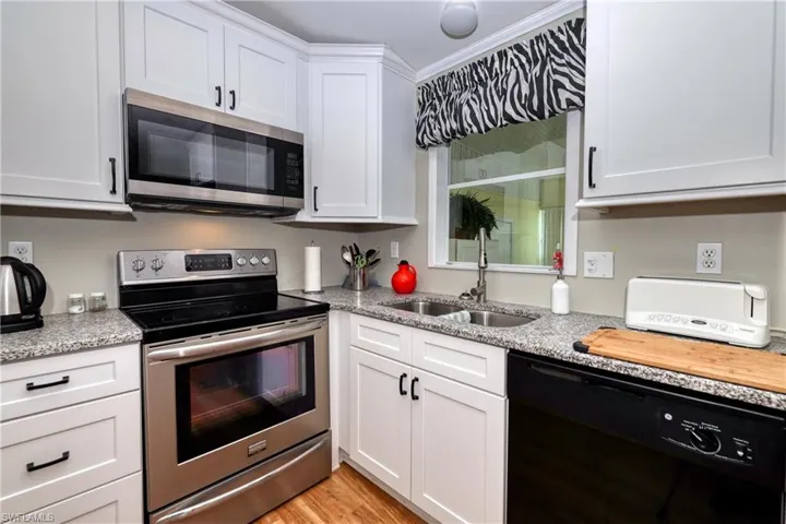 Kitchen with light stone countertops, white cabinetry, sink, stainless steel appliances, and light hardwood / wood-style floors