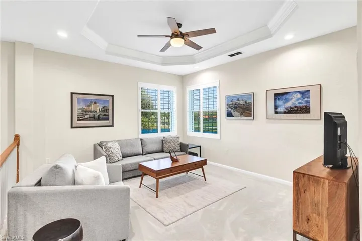 Carpeted living room with ceiling fan, ornamental molding, and a tray ceiling
