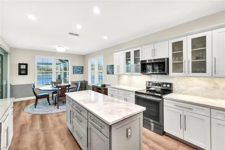 Kitchen with light wood-type flooring, tasteful backsplash, light stone counters, stainless steel appliances, and white cabinetry