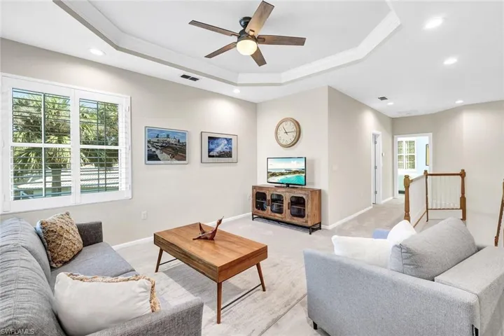 Carpeted living room featuring plenty of natural light, ceiling fan, a raised ceiling, and crown molding