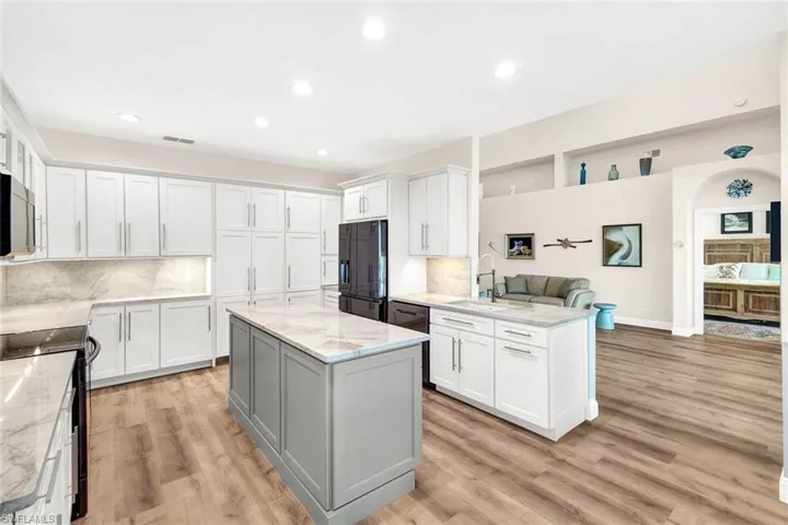 Kitchen featuring black appliances, white cabinets, sink, light hardwood / wood-style flooring, and light stone counters