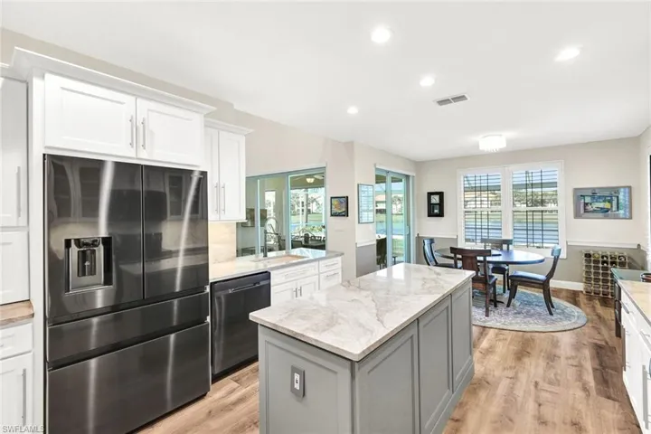 Kitchen with stainless steel fridge, a center island, sink, black dishwasher, and white cabinetry