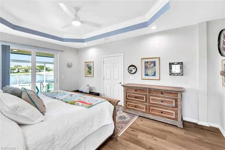 Bedroom with access to exterior, a raised ceiling, ceiling fan, crown molding, and wood-type flooring