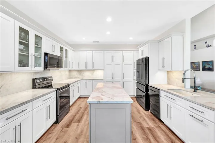 Kitchen with light stone countertops, light wood-type flooring, sink, black appliances, and white cabinetry