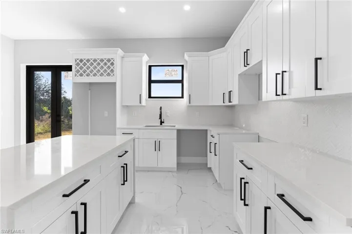 Kitchen featuring light stone countertops, white cabinetry, a center island, recessed lighting, and french doors