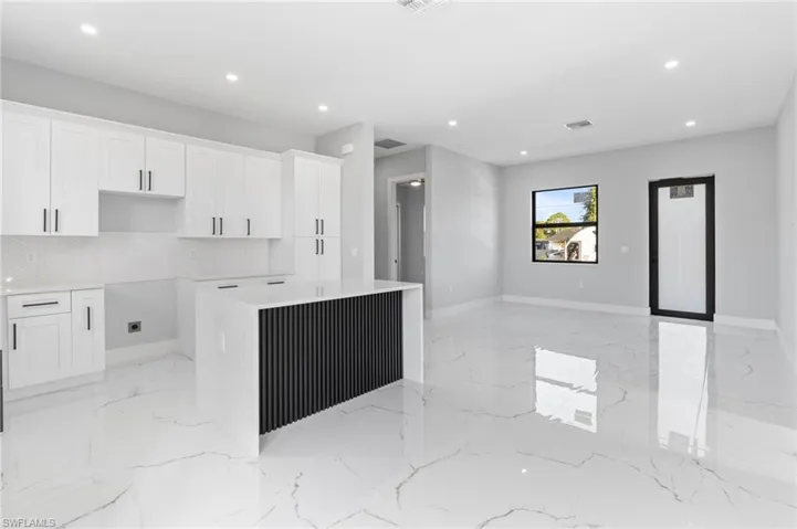 Kitchen with white cabinets, recessed lighting, light stone countertops, a kitchen island, and light marble finish floors
