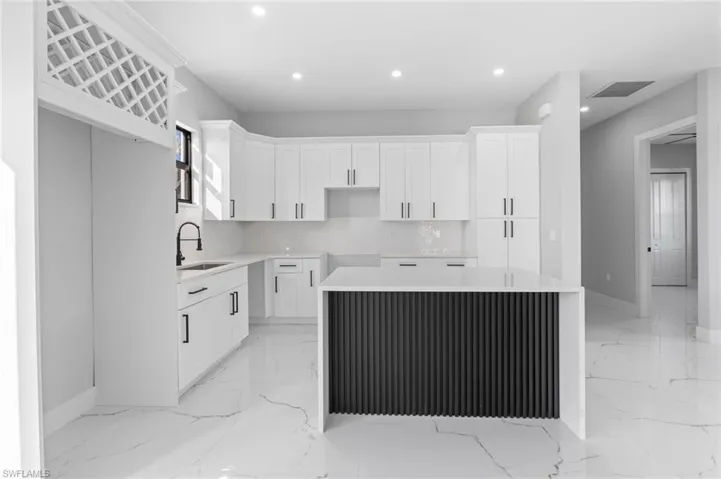 Kitchen featuring white cabinetry, recessed lighting, light stone countertops, light marble finish flooring, and a kitchen island