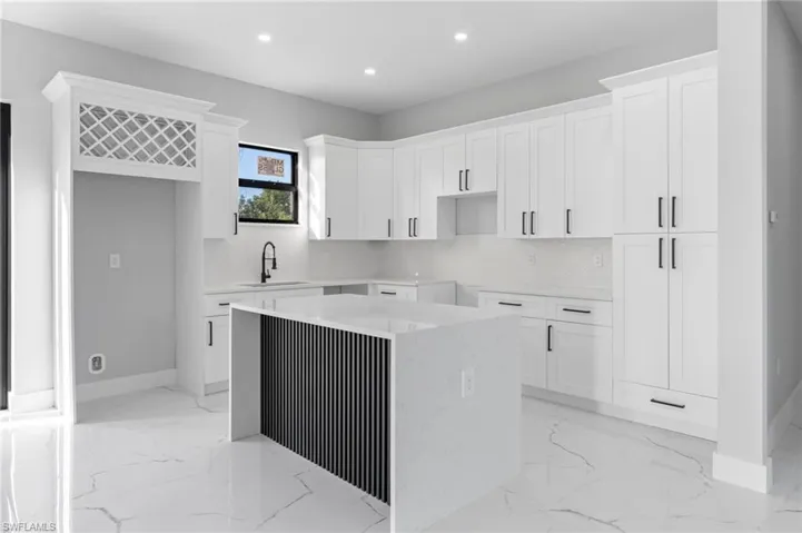 Kitchen with white cabinetry, recessed lighting, light stone countertops, a kitchen island, and light marble finish floors