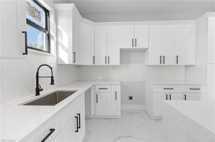 Kitchen featuring light stone countertops, white cabinetry, light marble finish floors, and backsplash