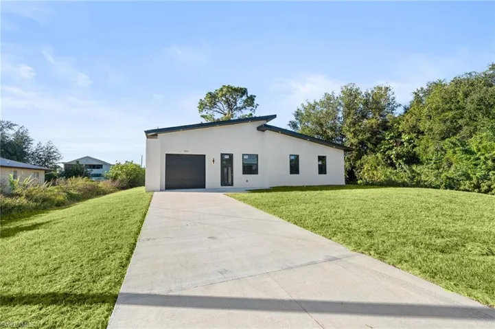 View of front of home featuring driveway, a front lawn, a garage, and stucco siding