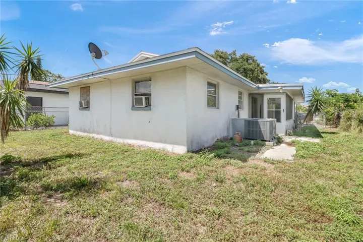 Rear view of house featuring central AC unit and a lawn