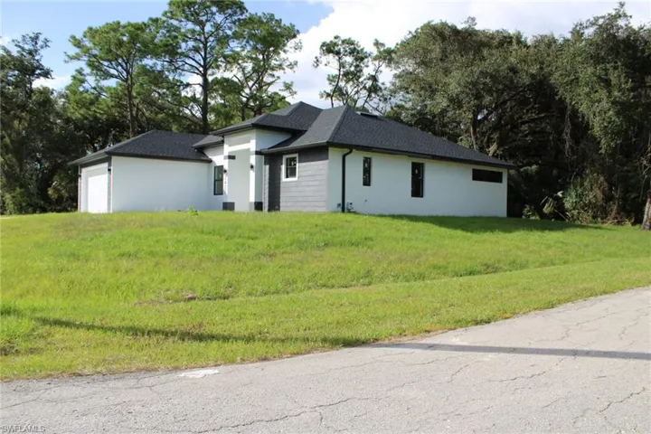 Single-story residence featuring a hipped roof, smooth stucco and stone veneer exterior, attached garage, and surrounding mature trees