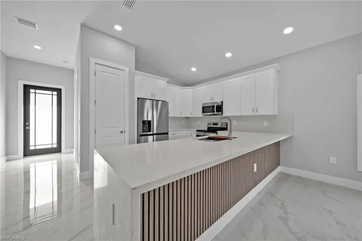 Kitchen featuring light stone counters, sink, white cabinetry, kitchen peninsula, and appliances with stainless steel finishes
