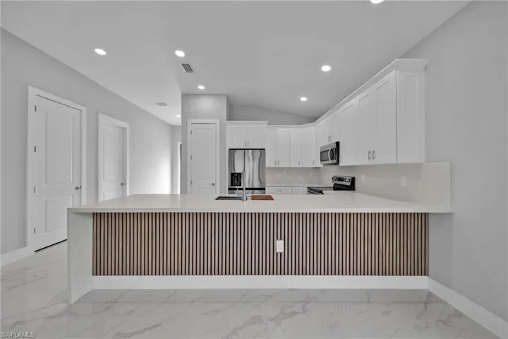 Kitchen featuring sink, lofted ceiling, white cabinetry, kitchen peninsula, and stainless steel appliances
