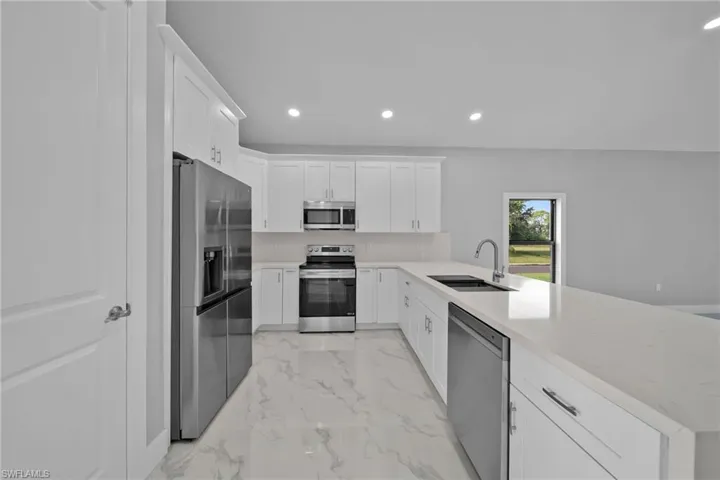 Kitchen with sink, kitchen peninsula, white cabinetry, stainless steel appliances, and light stone countertops