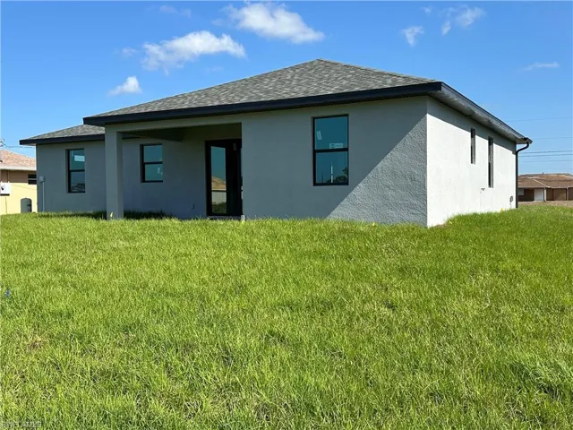 Back of house featuring a lawn, stucco siding, and roof with shingles