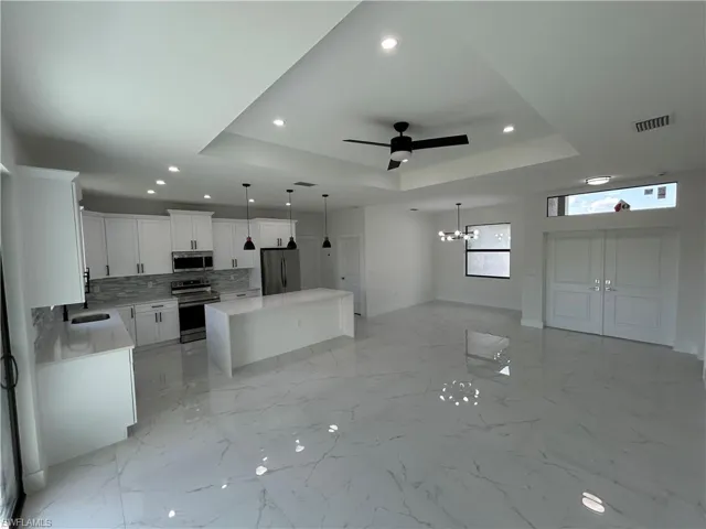 Kitchen featuring a sink, a raised ceiling, appliances with stainless steel finishes, open floor plan, and visible vents