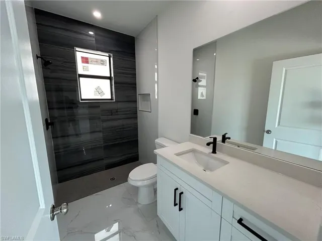 Full bath featuring vanity, marble finish floor, toilet, and tiled shower