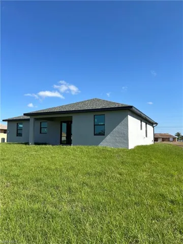 Rear view of house with a lawn and stucco siding