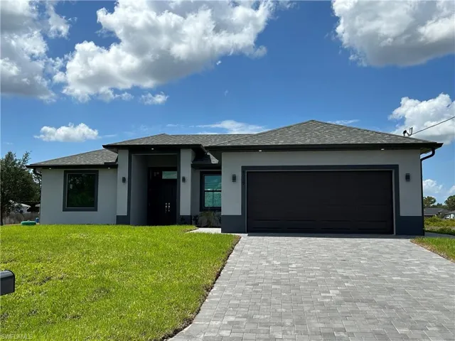 Prairie-style home featuring decorative driveway, an attached garage, a front yard, and stucco siding