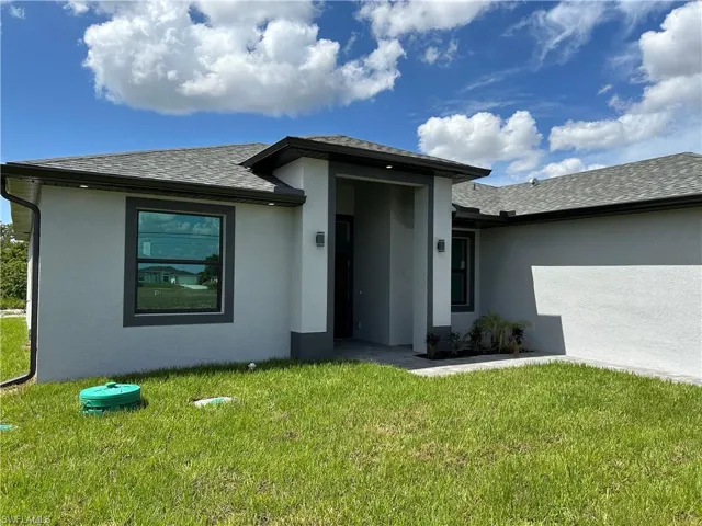 View of front of property featuring roof with shingles, stucco siding, and a front yard