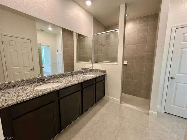 Full bath featuring a walk in shower, double vanity, tile patterned floors, baseboards, and recessed lighting
