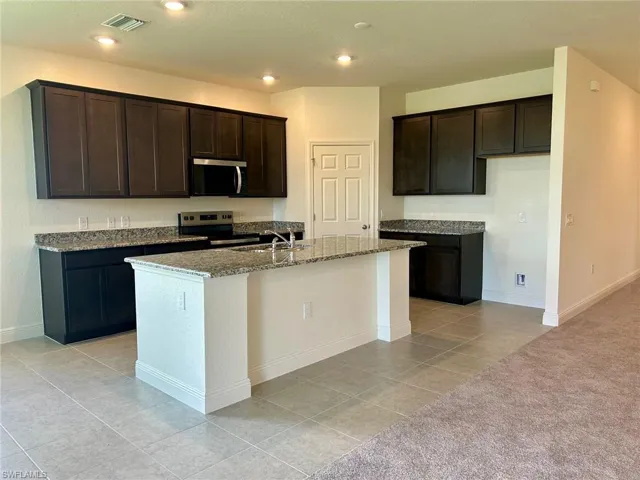 Kitchen featuring appliances with stainless steel finishes, dark stone counters, a center island with sink, dark brown cabinetry, and light tile patterned flooring