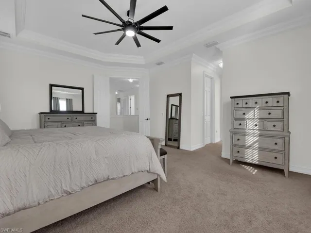 Bedroom with crown molding, a raised ceiling, light carpet, and ceiling fan