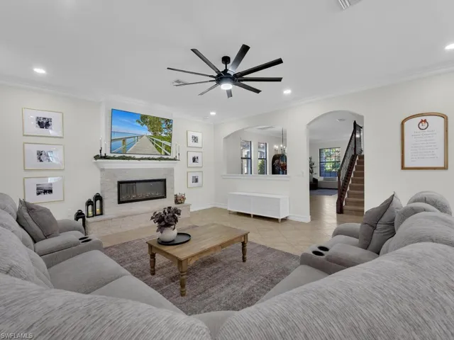 Tiled living area with arched walkways, crown molding, a glass covered fireplace, a ceiling fan, and recessed lighting
