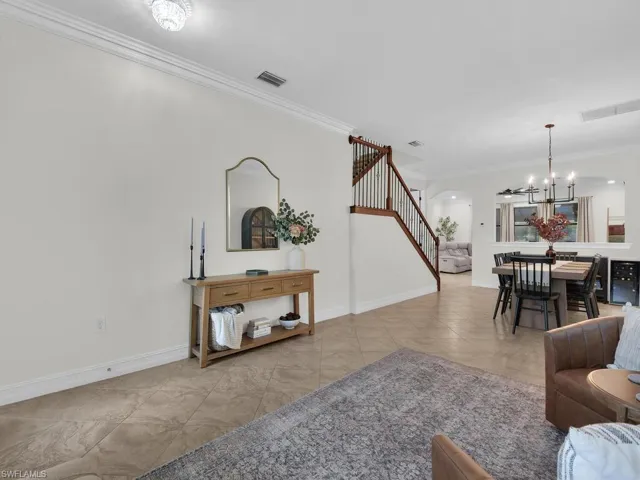 Living room with ornamental molding, suspended lighting, and arched walkways